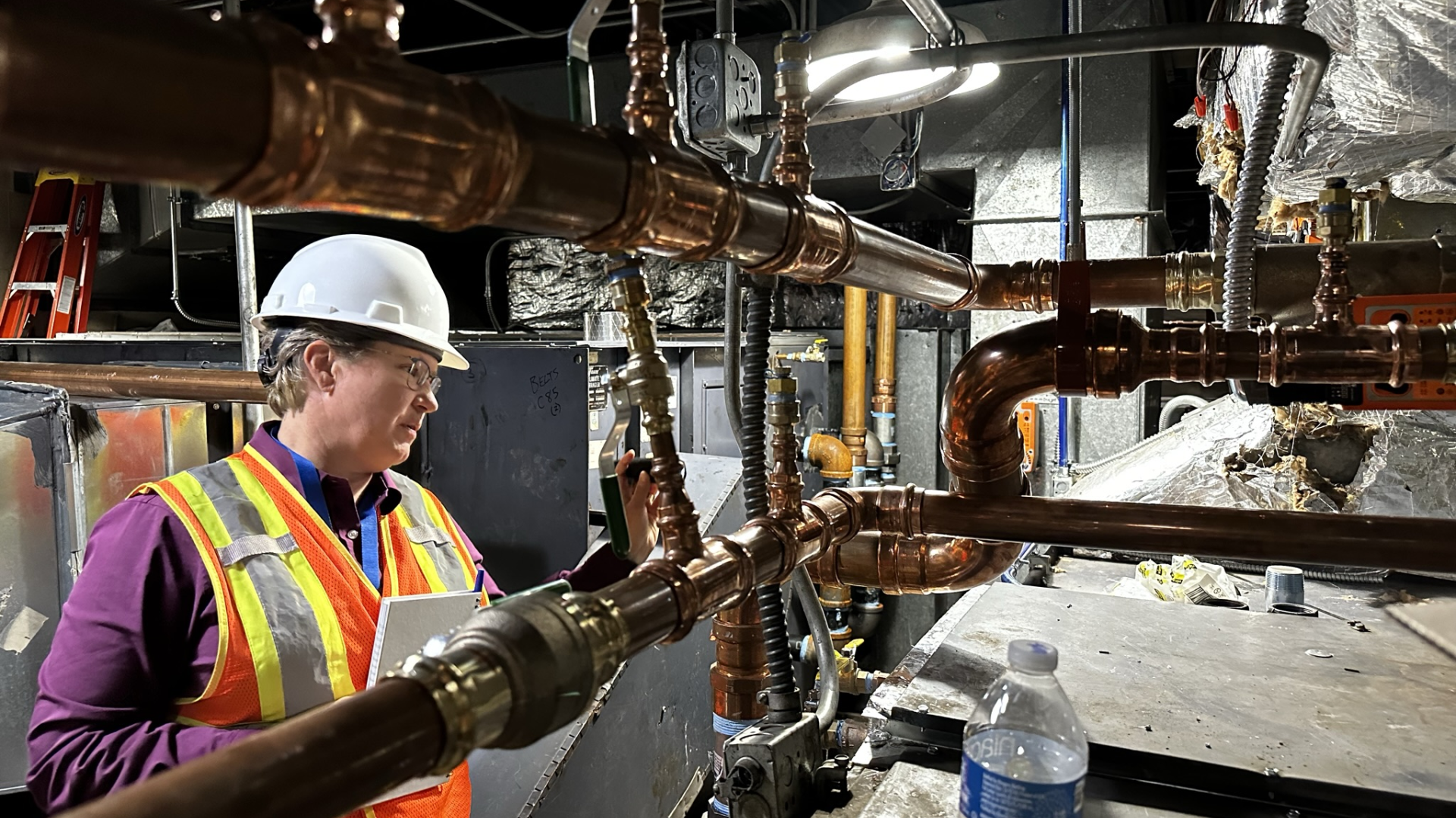 Owner Denies in a hardhat and safety vest in the mechanical equipment room at Denver Public School's Ford Elementary.