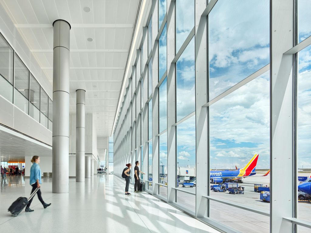 View from inside Denver International Airport looking out floor to ceiling windows at an airplane parked at a gate.