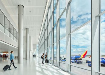 View from inside Denver International Airport looking out floor to ceiling windows at an airplane parked at a gate.