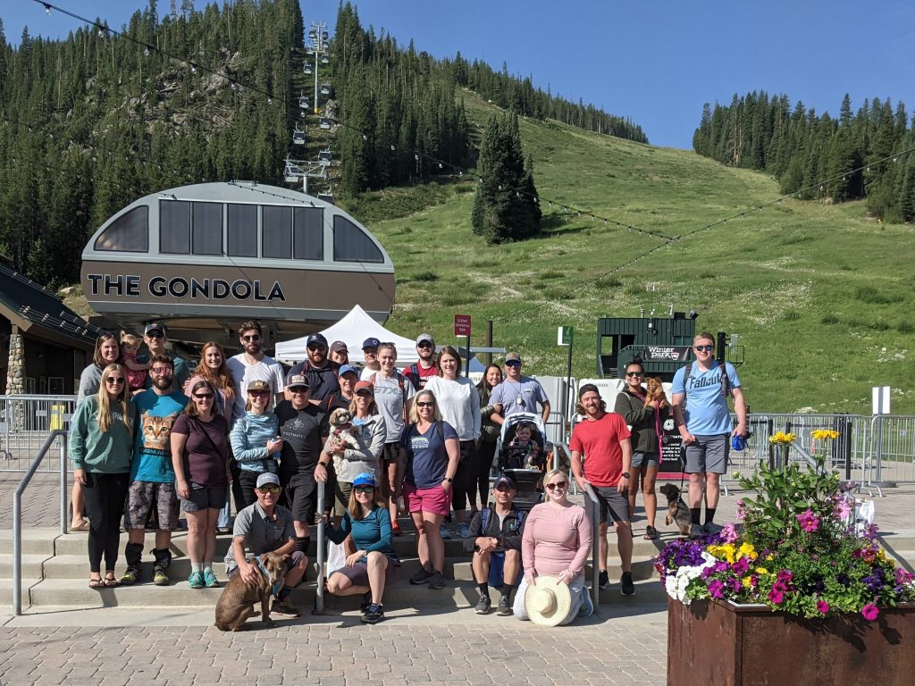 Team in front of gondola on summer green mountain.