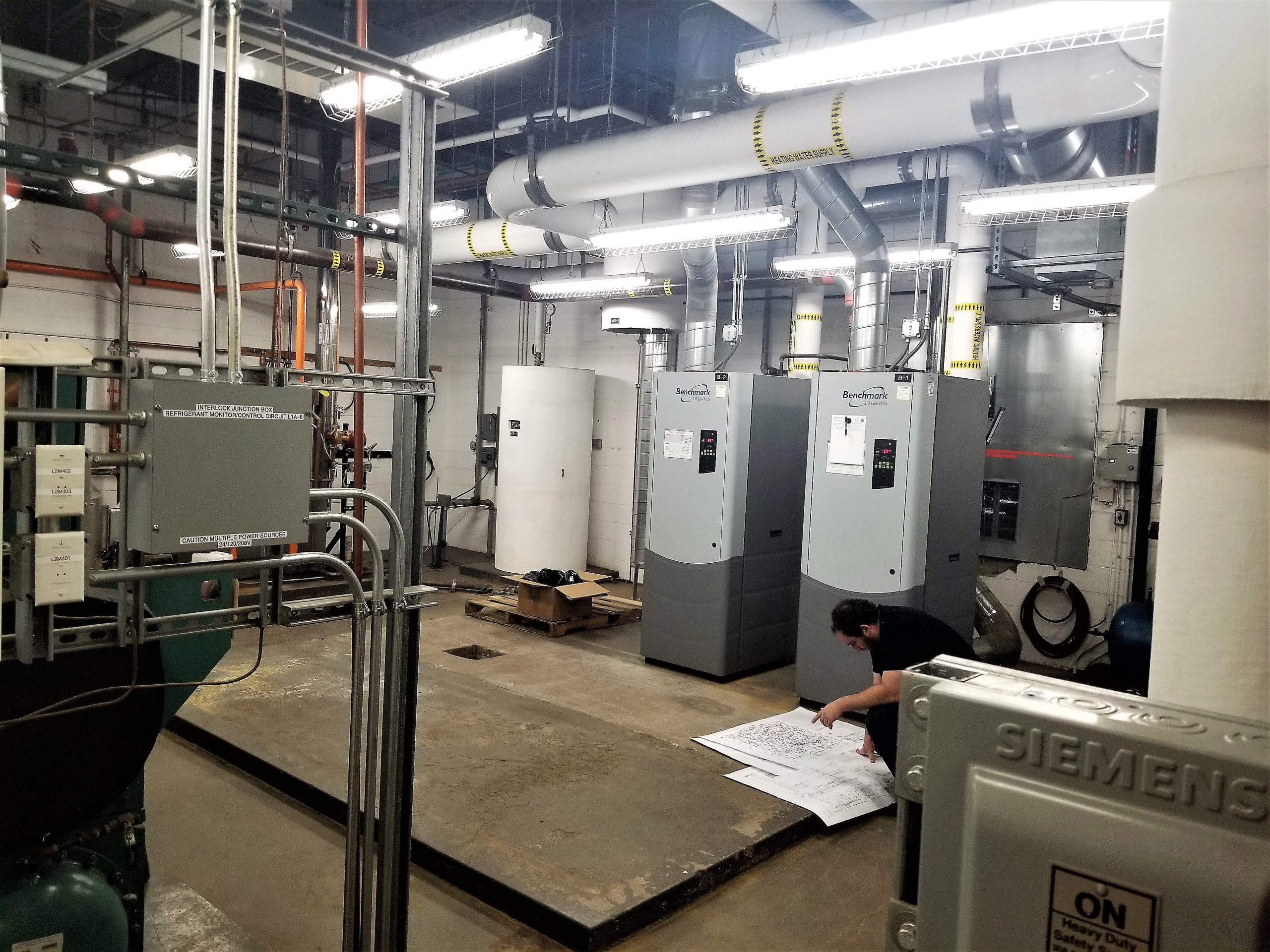 Mechanical equipment room at Holm Elementary in Denver, CO with engineer reviewing plans in the forground.