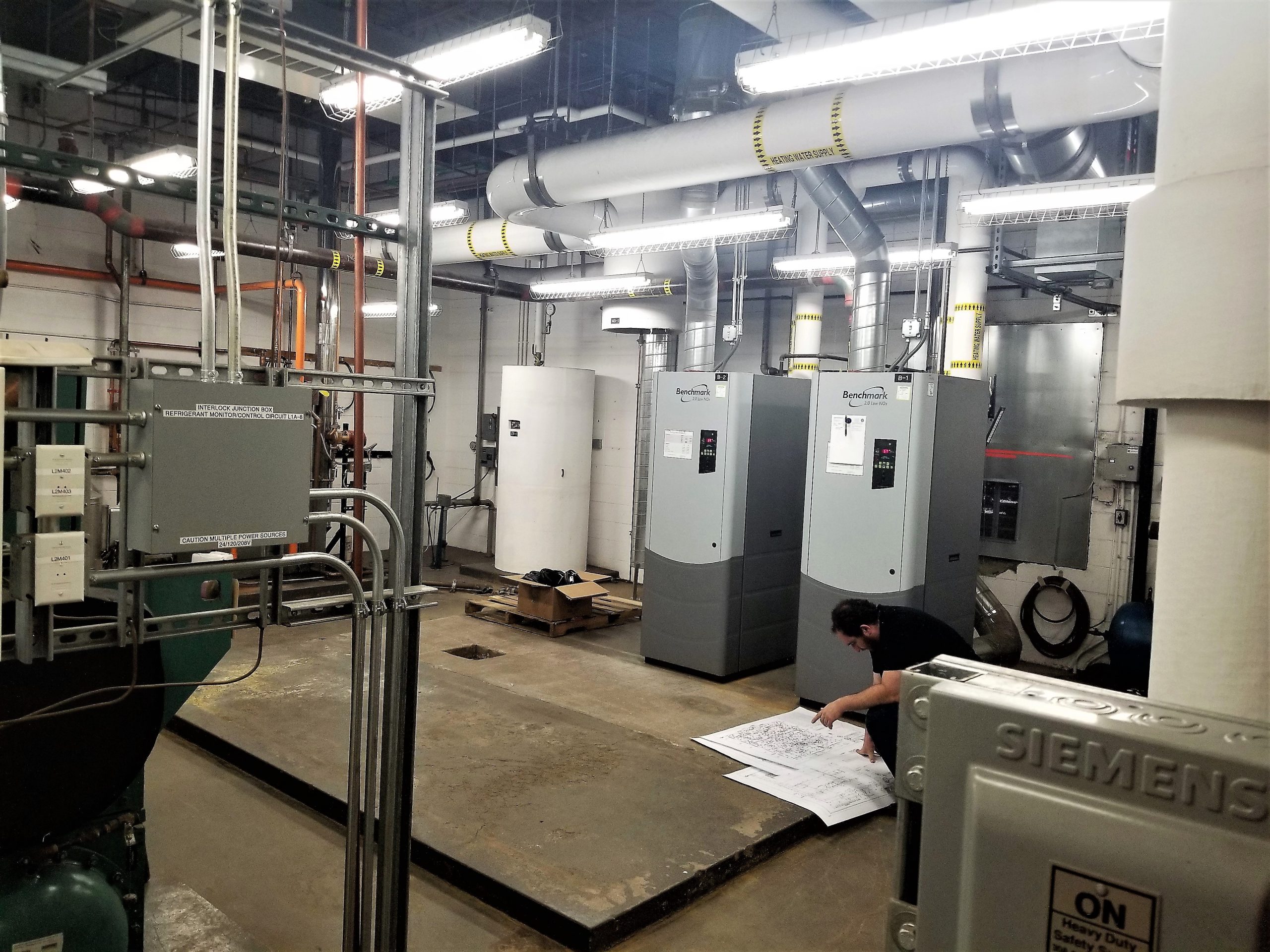 Mechanical equipment room at Holm Elementary in Denver, CO with engineer reviewing plans in the forground. 